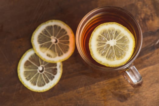 Top view of black tea with lemon in cup and on wooden plank table.