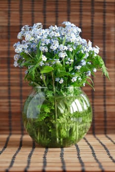 Bunch of blue wildflowers in glass vase on wooden background