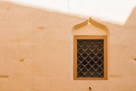 Orange well preserved wall with a window with an arch. Former capital of Malta - Mdina. Fusion of arabian architecture and baroque.