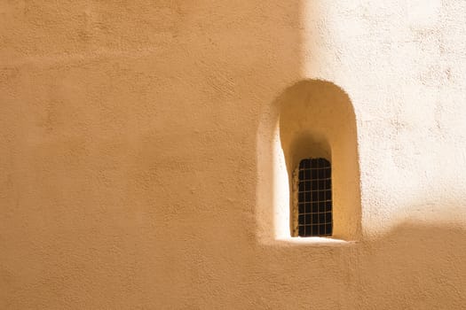 Facade of an old house with an old window with an arch in arabian style. Wall partly enlightened by the sunlight. Former capital of Malta - Mdina.