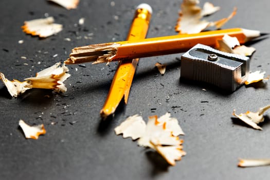 Broken pencil with metal sharpener and shavings on black background. Horizontal image.