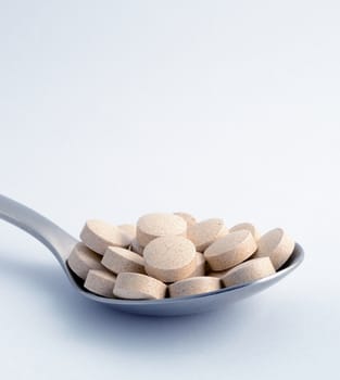 Macro shot of brown tablets at the spoon, grey background. 