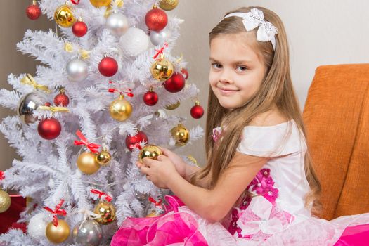 Seven-year girl in a beautiful dress treats Christmas toys and looked into the frame
