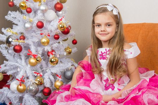 Seven-year girl sitting on a sofa in a beautiful dress the Christmas tree