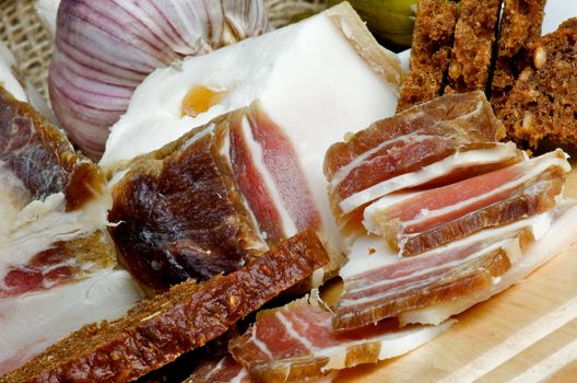 Homemade Raw Smoked Bacon Full Body and Slices with Garlic and Brown Bread closeup on Cutting Board