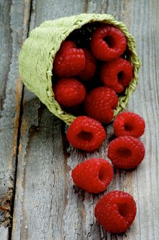 Fresh Raw Sweet Raspberries into Green Wicker Basket closeup on Rustic Wooden background