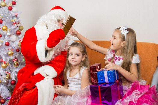 Santa Claus gives gifts to one girl, the other sitting in the waiting