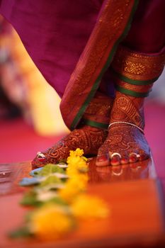 The feet of a bride during a traditional Indian wedding ritual of stepping over flowers.