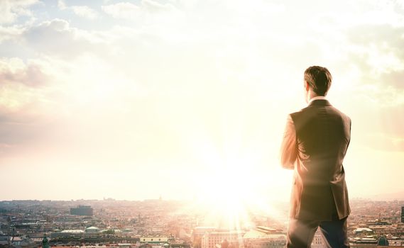 Young businessman standing on edge of rock mountain and looking at city