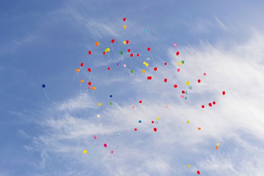 Multicolored balloons flying in blue sky with white clouds