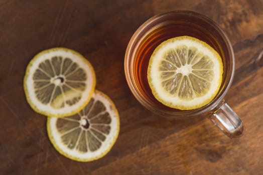 Top view of black tea with lemon in cup and on wooden plank table.