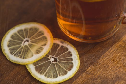 Top view of black tea with lemon in cup and on wooden plank table.