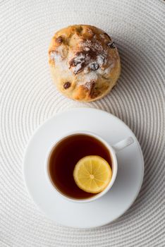 Homemade carrot muffin with cap of tea and lemon on white fabric background. top view