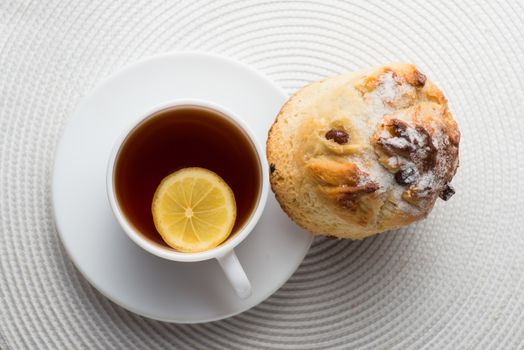 Homemade carrot muffin with cap of tea and lemon on white fabric background. top view