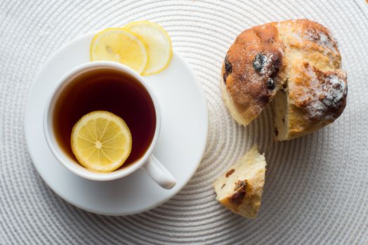 Homemade carrot muffin with cap of tea and lemon on white fabric background. top view