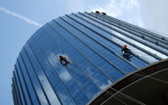 Group of Asian construction worker working on highrise building, Vietnamese man climb on rope and clean glass surface of skyscraper, a dangerous job of industry service