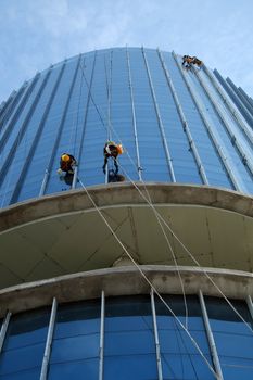 Group of Asian construction worker working on highrise building, Vietnamese man climb on rope and clean glass surface of skyscraper, a dangerous job of industry service
