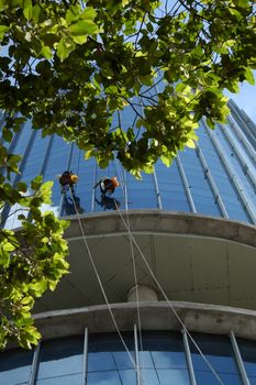 Group of Asian construction worker working on highrise building, Vietnamese man climb on rope and clean glass surface of skyscraper, a dangerous job of industry service