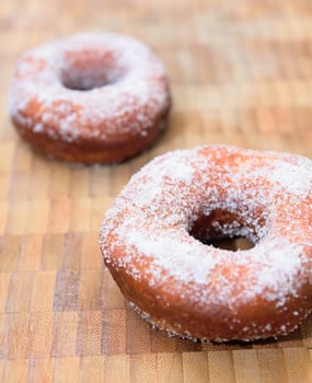 Sweet donuts sprinkled with sugar on wooden tray.