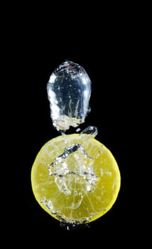 Lemon falling into water with splashing water and bubbles on a black background.