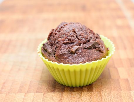 Chocolate muffin in the yellow silicone form on a wooden plate.