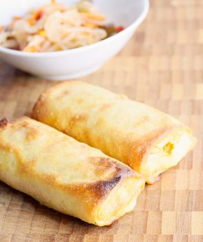 Chinese spring rolls on a wooden plate with vegetable salad.