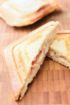 Baked toast with ham and cheese on a wooden plate.