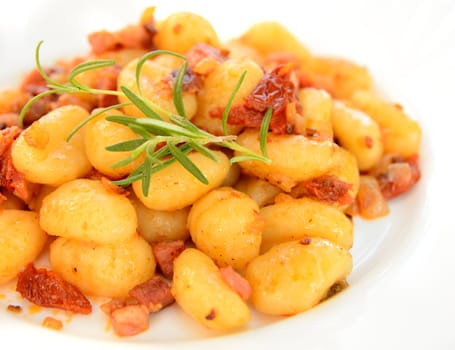 Gnocchi with tomatoes, bacon and onion on the white plate.