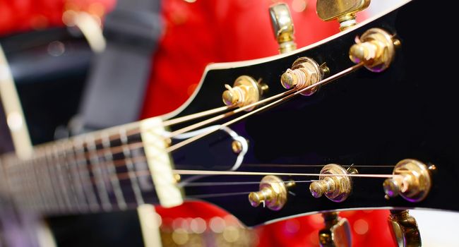 Musician in red dress holding and playing the electric guitar. Closeup of headstock.