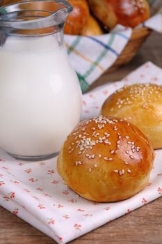 Buns with sesame seeds and a jug of milk on the table