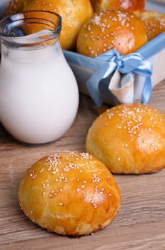 Buns with sesame seeds and a jug of milk on the table