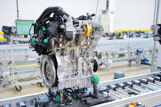 Newly manufactured engine on the production line in a factory. Behind the engine is computer on the desk.