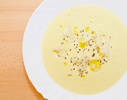 Top view on the table with cauliflower cream soup with olive oil, basil herbs and small whole cauliflowers.