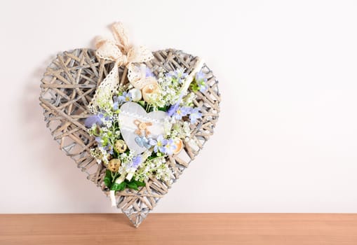 Easter floral home decoration on the table. Wicker heart, love symbol. Homemade arrangement.