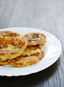 Fresh fried zucchini potato pancakes on a white plate on the wooden table.