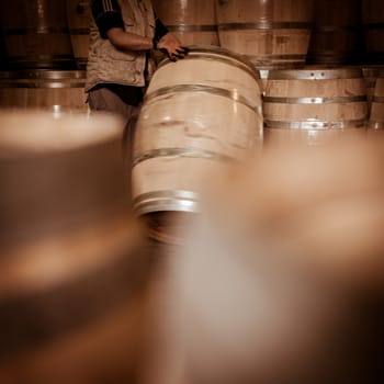 Winemaker barrels moving up or down by rolling on the ground in a large storage cellar, Bordeaux Vineyard, France