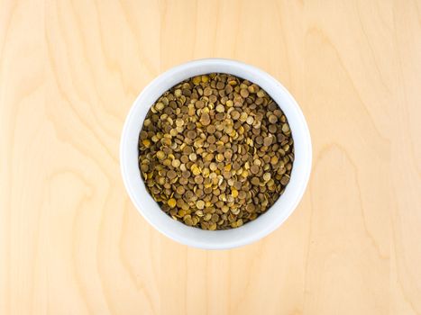 Pile of raw dry brown lentils in cup, top view, center composition, food preparation, copy space