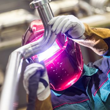 Industrial worker with protective mask welding inox elements in steel structures manufacture workshop.