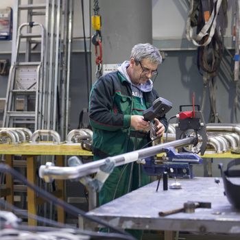 Industrial operator setting  computer controlled process of orbital welding machine in  stainless steel pipes manufacturing workshop.