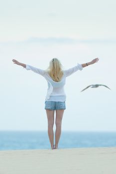 Woman enjoying freedom feeling as a bird at beach at dusk. Serene relaxing woman in pure happiness and elated enjoyment with arms raised outstretched up. 