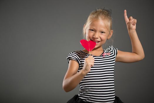 Pretty little girl smiling and posing with lollipop. Studio shutting. Grey background. Looking at camera.