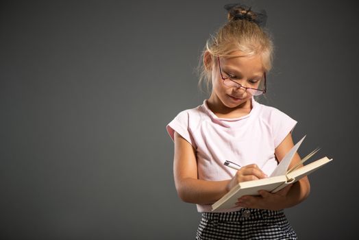 Tired Cute little girl standing and holding book. Studio shutting. Grey background. Looking at camera.