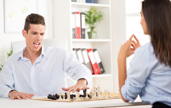 Young angry businessman of loses playing chess with businesswoman in the office.