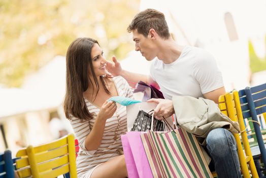 Young couple in the break after shopping at outdoor cafe watching the things they bought.