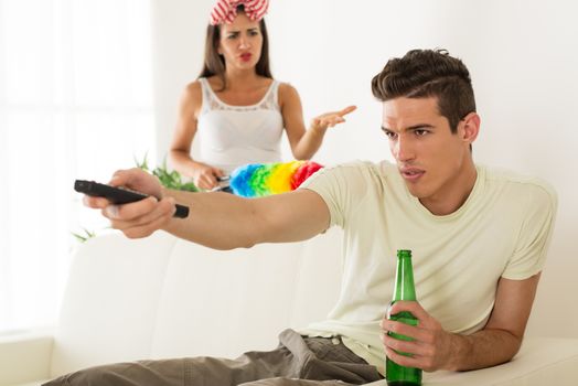 Young man sitting on sofa and watching tv. His angry wife yelling.