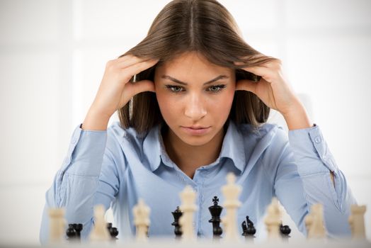 Young beautiful businesswoman devises Business strategy. She sitting above the chessboard with figures and thinking.