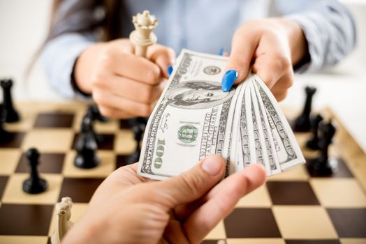 Business persons holding dollars above the chessboard