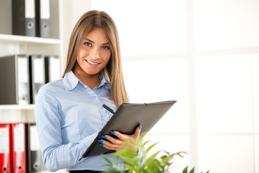 Beautiful Businesswoman with documents standing in the office and looking at camera.