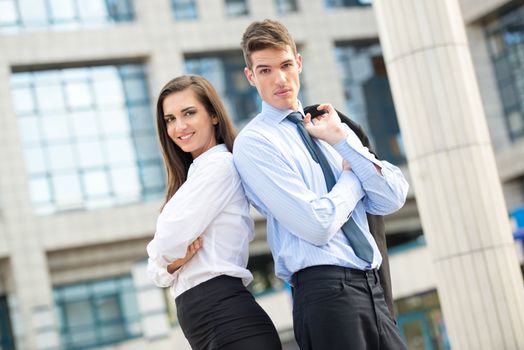 Young business couple standing in front of office building leaning back on each other.