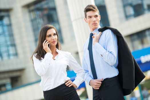 Young business couple standing in front of office buildings and business woman talking by mobile phone.